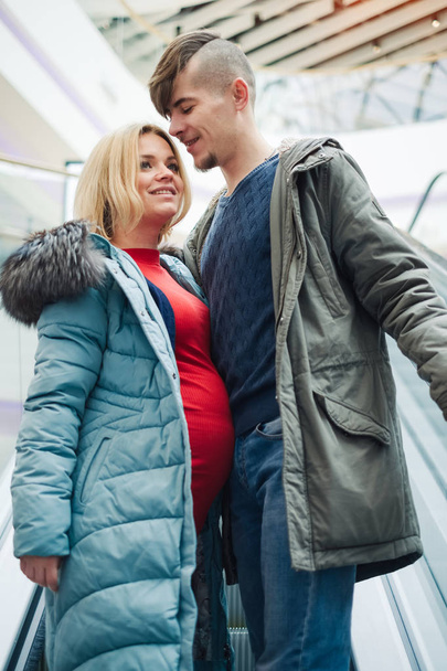 Beautiful pregnant couple walking in shopping center. Wife with husband enjoy spend time together. Young family love each other - Zdjęcie, obraz