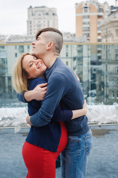 Beautiful pregnant family spend time together with winter view on city background. Young wife with husband enjoy love each other - Valokuva, kuva