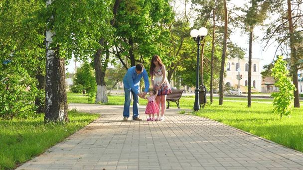 pequeño bebé aprendiendo a caminar con mamá y papá ayudándolo a dar sus primeros pasos, feliz familia caminando en el parque de verano
 - Foto, Imagen