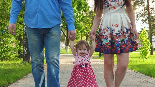 bebé aprendiendo a caminar con mamá y papá, familia feliz caminando en el parque de verano
 - Foto, Imagen