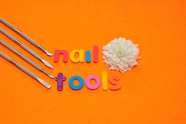 Een set nagel hulpmiddelen en een witte aster op een oranje achtergrond en het woord nagel hulpmiddelen - Foto, afbeelding