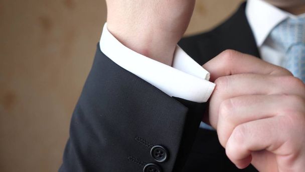 l'uomo in cravatta blu e vestito nero raddrizza la manica di una camicia bianca
. - Foto, immagini
