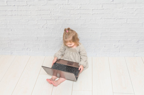 девушка, детская деловая женщина, работающая за ноутбуком, напротив стены из белого кирпича
 - Фото, изображение
