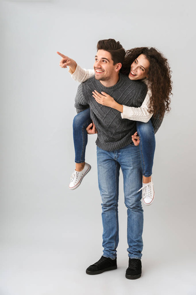 Image of young couple having fun and while man piggybacking woman isolated over gray background - Photo, image