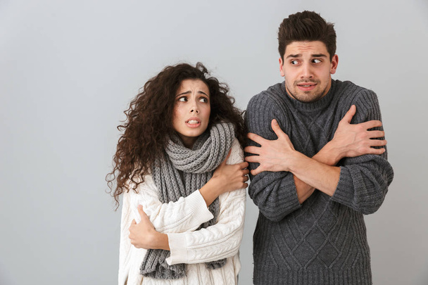Photo of displeased couple man and woman wearing scarfs trembling and hugging themselves isolated over gray background - 写真・画像