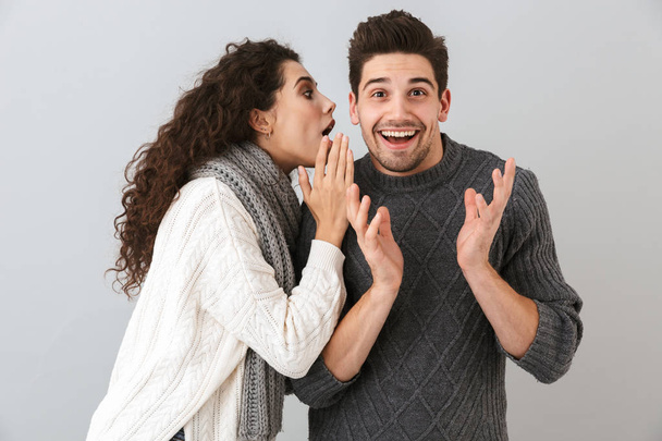Portrait of excited woman talking to her boyfriend in his ear isolated over gray background - Photo, Image