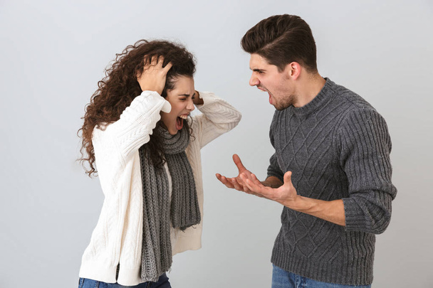 Photo of displeased man and woman screaming at each other standing face to face isolated over gray background - Foto, Imagen