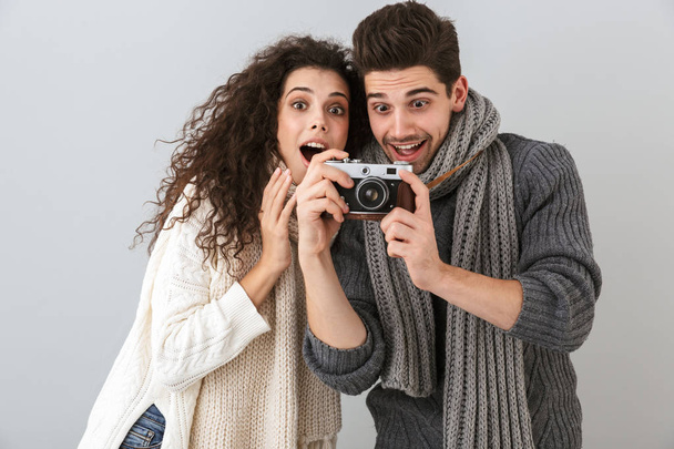 Image of excited couple man and woman smiling while holding retro camera isolated over gray background - Valokuva, kuva