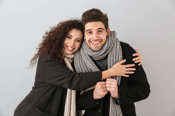 Happy couple wearing autumn clothes standing isolated over gray background, hugging - 写真・画像