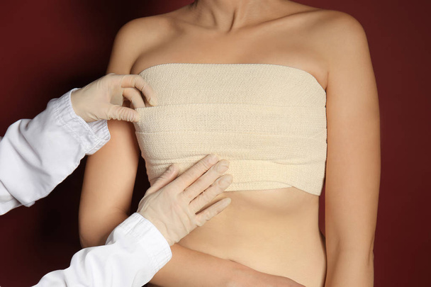 Doctor applying bandage on female chest after cosmetic surgery operation against color background - Zdjęcie, obraz