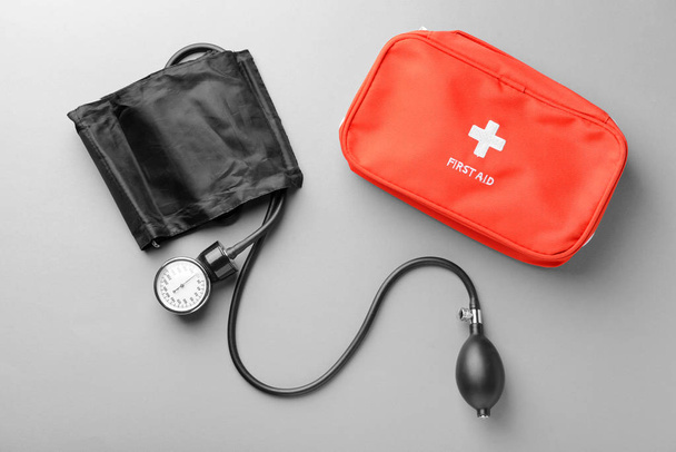 Sphygmomanometer and first aid kit on grey background. Health care concept - Zdjęcie, obraz