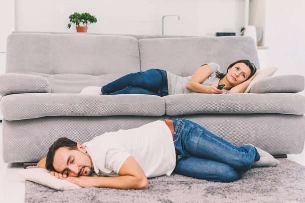 Чоловік спить на підлозі, а його дружина дивиться телевізор
 - Фото, зображення