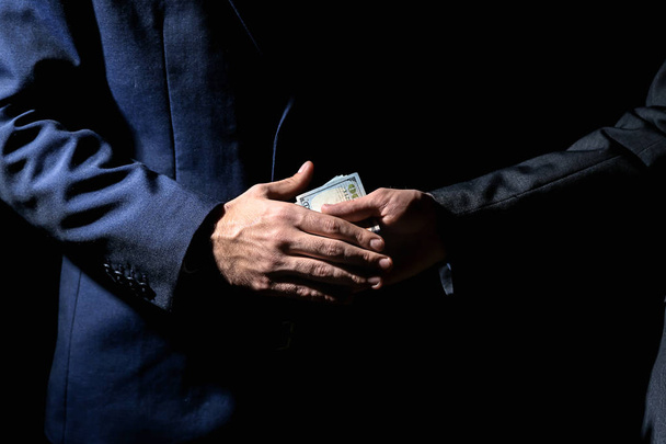 Zakenman nemen van smeergeld van man tegen de donkere achtergrond. Concept van corruptie - Foto, afbeelding