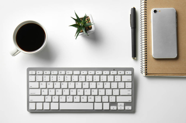 Teclado do computador, notebook, telefone, xícara de café e suculento na mesa branca
 - Foto, Imagem