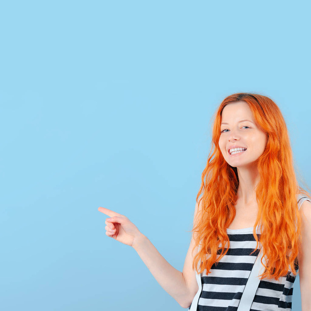 Rapariga ruiva sorri e aponta com o dedo indicador. Modelo de promoção e demonstração de bens
 - Foto, Imagem