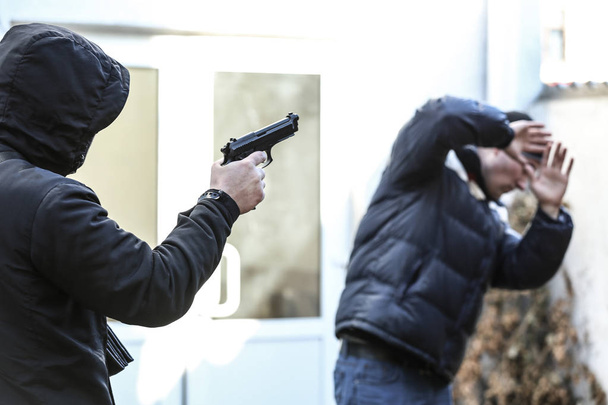 Armed bandit aiming at helpless victim outdoors - Fotó, kép