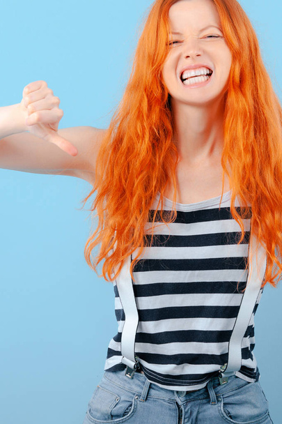 Red-haired girl frowns, grins and shows thumb down. Negative and Condemnation - Fotoğraf, Görsel