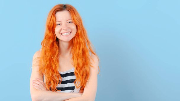 Red-haired girl smiles, having combined hands on breast on blue background. Positive and approval - 写真・画像
