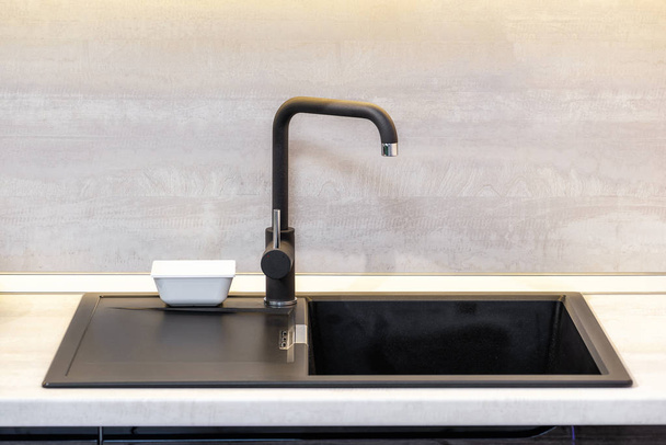 schwarze Keramikspüle und Mischbatterie auf hölzerner Arbeitsplatte in der Küche. - Foto, Bild