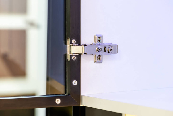 Close-up van een instelbare verborgen scharnier gefixeerd op een kast met een glazen deur. - Foto, afbeelding