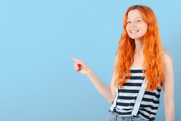 Rapariga ruiva sorri e aponta com o dedo indicador. Modelo de promoção e demonstração de bens
 - Foto, Imagem