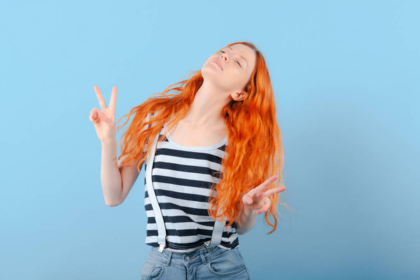 Red-haired girl closed her eyes and shows two fingers. Positive, success, bliss and enjoyment - Fotoğraf, Görsel