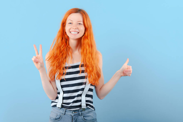Red-haired girl smiles and shows two fingers. Positive and success - Foto, Imagen
