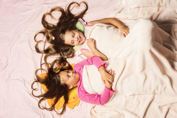 Kids in pink pajamas under white blanket. Children with smiles - Fotografie, Obrázek