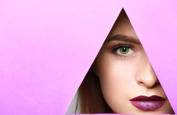 Όμορφη νεαρή γυναίκα που αναζητούν μέσα από το τρίγωνο σε σχήμα τρύπα στο χρώμα χαρτιού - Φωτογραφία, εικόνα