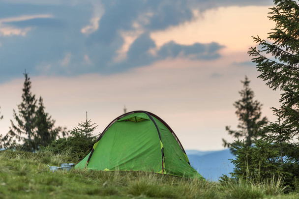 遠い霧青山、日の出や日没の背景の前に明確なピンクの空の草で覆われた丘の上のテントを観光。夏は夜明けに山でキャンプします。観光、ハイキング、自然概念の美しさ. - 写真・画像
