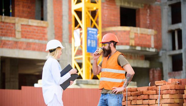 Woman engineer and brutal builder communicate construction site background. Construction team communication concept. Relationships between construction clients and participants building industry - Фото, зображення