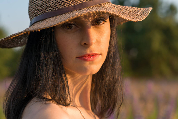 Portrait of a young, sympathetic, sexy girl in a woman's crimson wicker hat at sunset in the field of lupine - Photo, Image