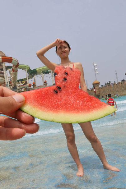A tourist poses behind a piece of watermelon to make an illusion of a watermelon "dress'' at 37 Degree Dream Sea Park in Yantai city, east China's Shandong province, 4 July 2017 - Фото, зображення