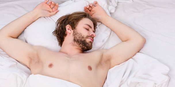 Picture showing young man stretching in bed. Young man stretching while waking up in the morning. Man with eyes still closed reaching button on the clock to turn it off. - Fotoğraf, Görsel