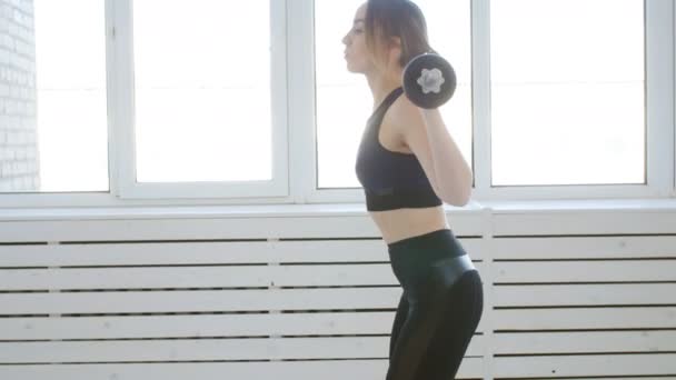 Home fitness concept. Jonge vrouw met een barbell doet oefeningen in een wit interieur - Video