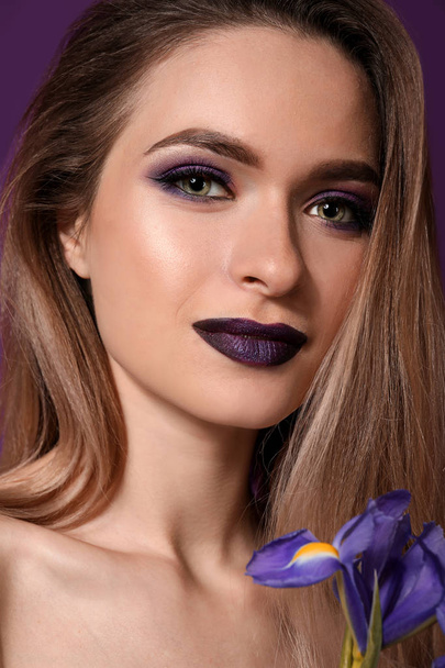 Hermosa mujer joven con maquillaje en tonos violeta y flor sobre fondo de color
 - Foto, Imagen