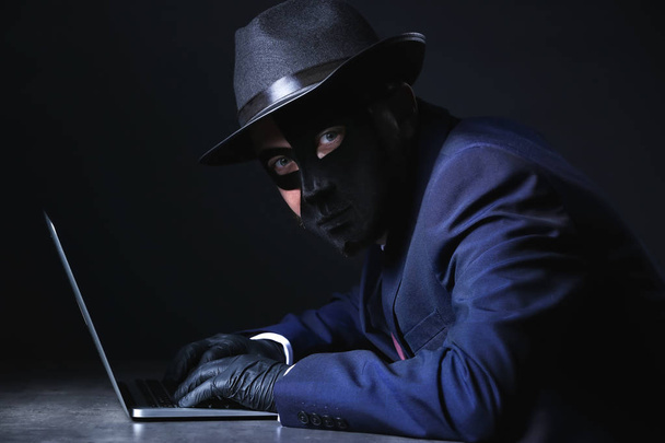 Ammattimainen hakkeri kannettavan istuu pöydässä tummalla taustalla
 - Valokuva, kuva