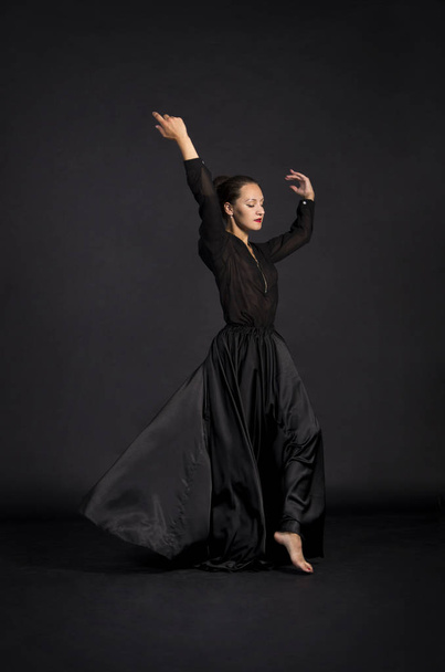 A young,smiling girl in black suit dancing modern choreography.Studio shot on dark background, isolated image. - Foto, imagen