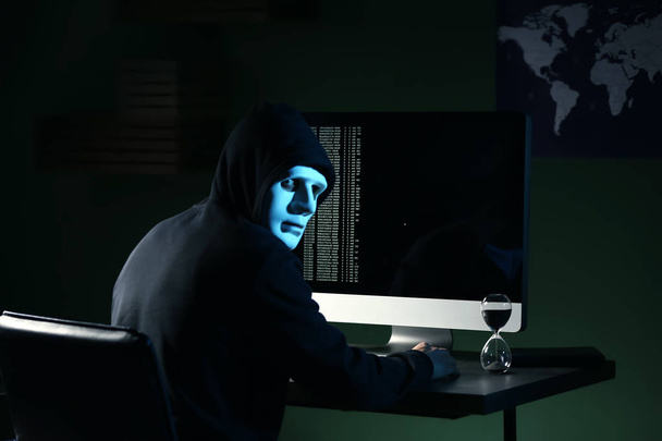 Professional hacker in mask using computer in dark room - Photo, Image