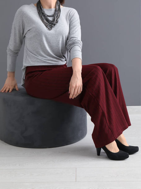 Bella giovane donna elegante seduta sul pouf vicino al muro grigio
 - Foto, immagini