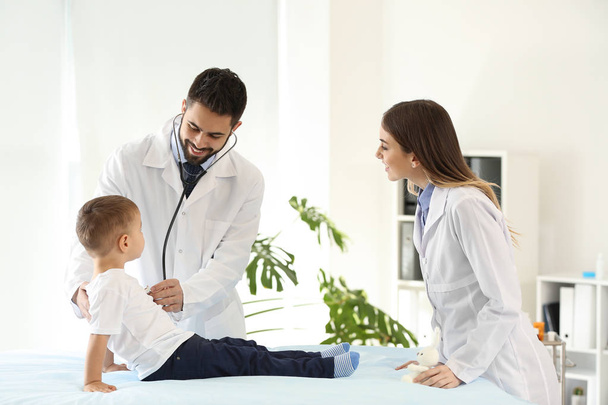Αρσενικό ο γιατρός με τον συνάδελφό του εργάζονται με χαριτωμένο μικρό αγόρι στην κλινική - Φωτογραφία, εικόνα