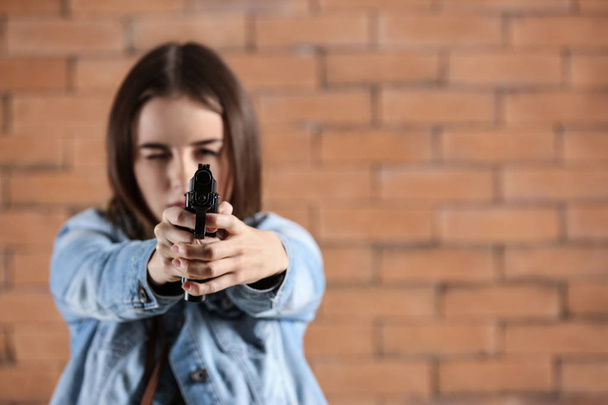 joven mujer apuntando un arma al espectador contra el fondo de ladrillo
 - Foto, Imagen