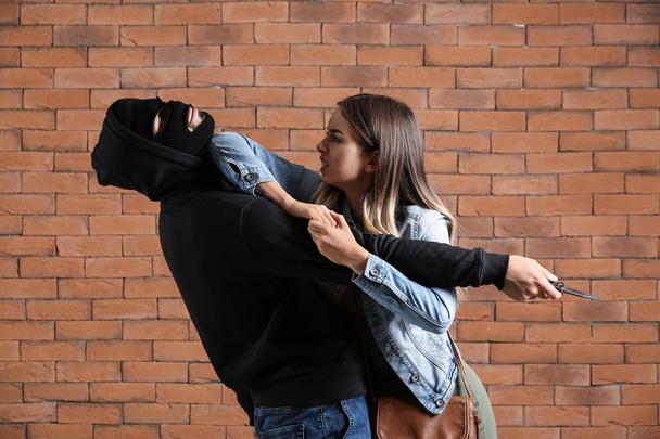 Mujer joven defendiéndose del ataque de bandido masculino contra fondo de ladrillo
 - Foto, Imagen