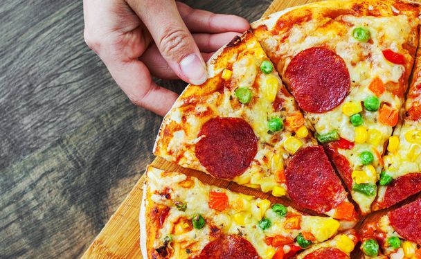 woman Hand toma una rebanada de pizza con mezcla de verduras, queso Mozzarella, pepperoni, tomate, salami. Pizza italiana sobre fondo de madera
 - Foto, Imagen