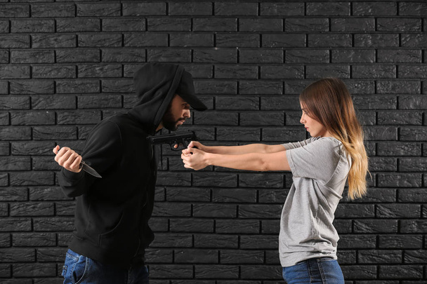 Mujer joven defendiéndose del ataque de bandido masculino contra fondo de ladrillo oscuro
 - Foto, Imagen