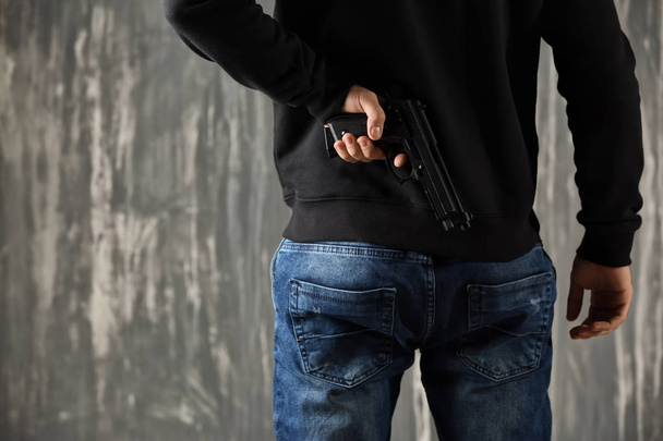 Male criminal with gun on grey background - Фото, изображение