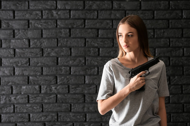 Young woman with a gun on dark brick background - Foto, imagen