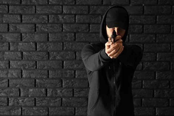 Чоловічий злочинець, який вказує на пістолет у спостерігача на тлі темної цегли
 - Фото, зображення