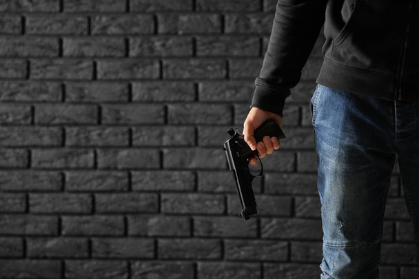 Αρσενικό ποινικής με ένα πυροβόλο όπλο σε φόντο σκοτεινό τούβλο - Φωτογραφία, εικόνα