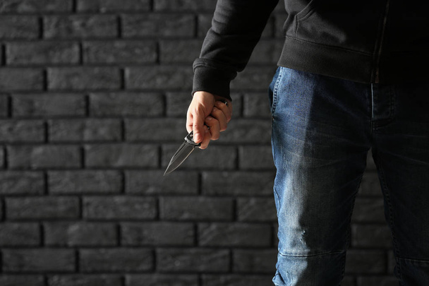 Male criminal with a knife on dark brick background - Foto, Bild